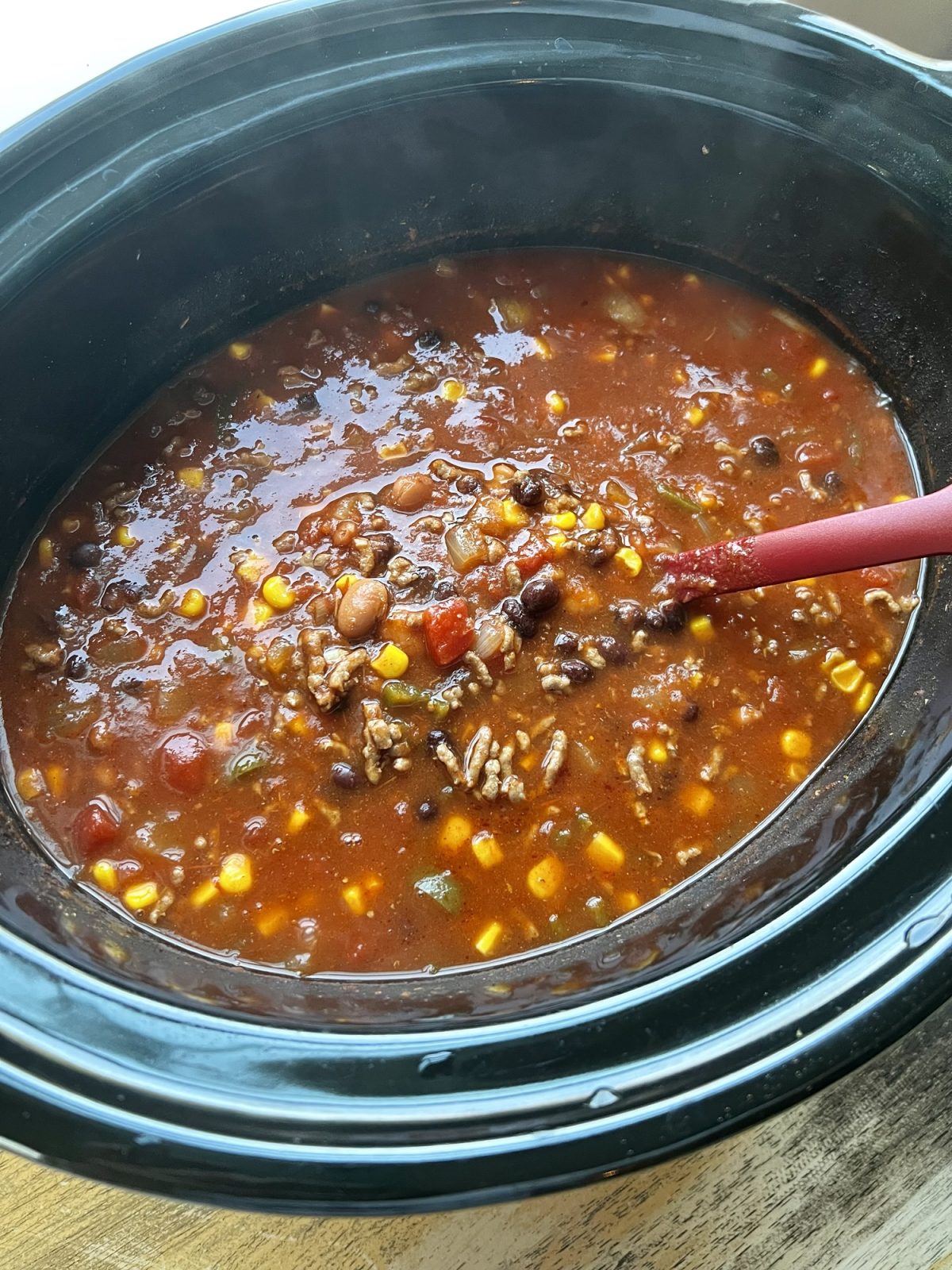 Crockpot taco soup in a large crockpot on a wooden table, with a red spoon scooping some