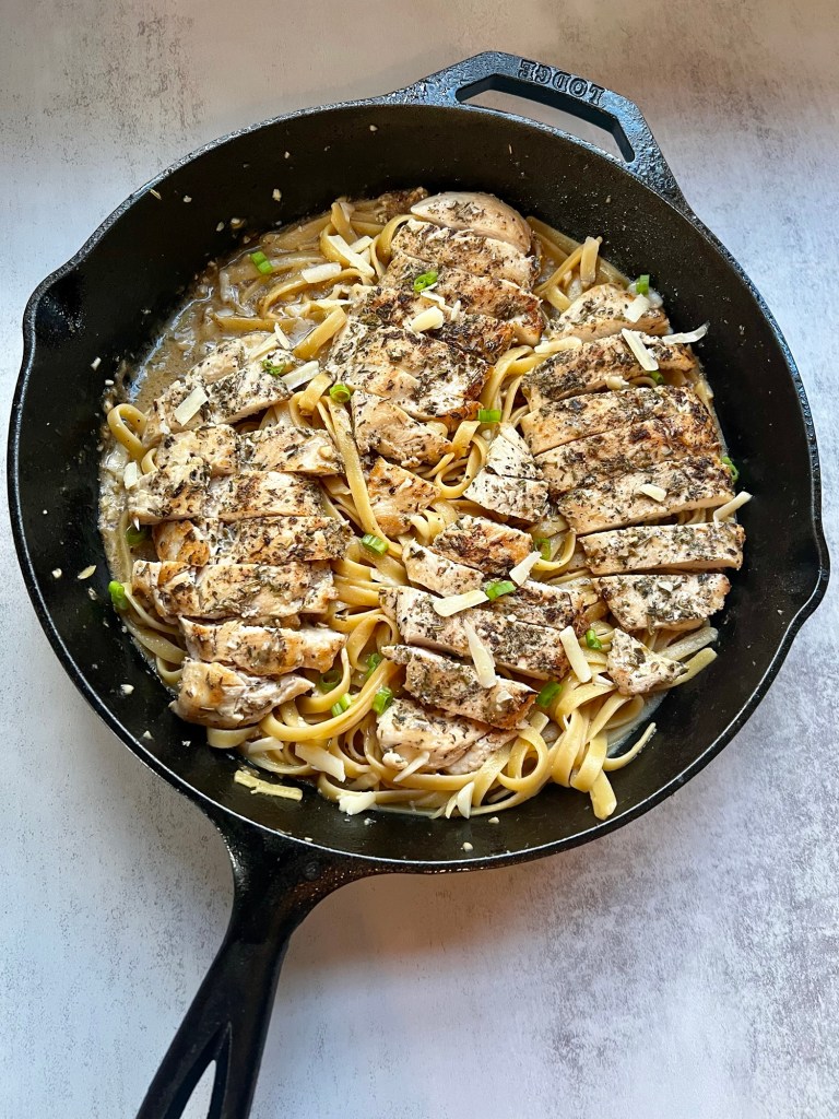 Garlic chicken pasta with green onion and parmesan for garnish in a cast iron skillet sitting on a countertop