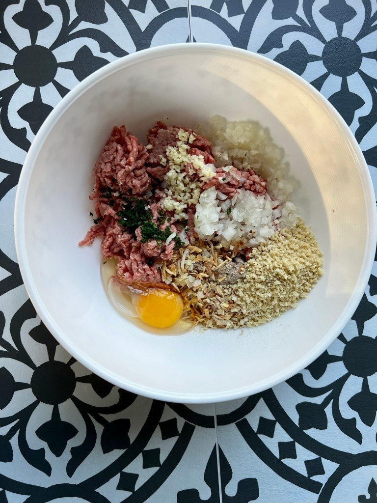 A mixing bowl filled with burger patty ingredients before being mixed