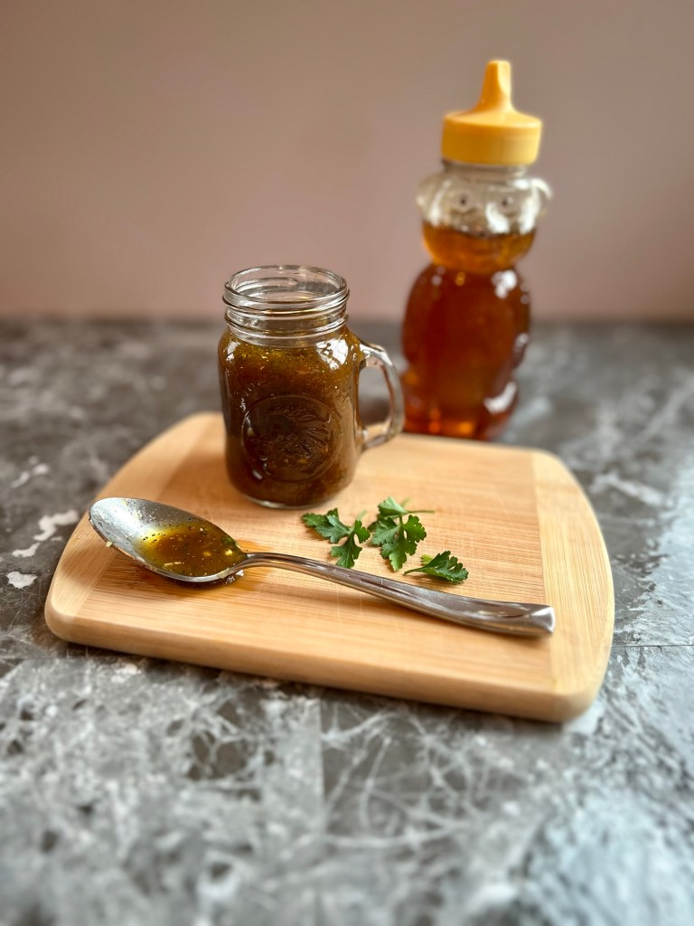 Honey balsamic vinaigrette in a small jar with a spoonful of it and some herbs next to it