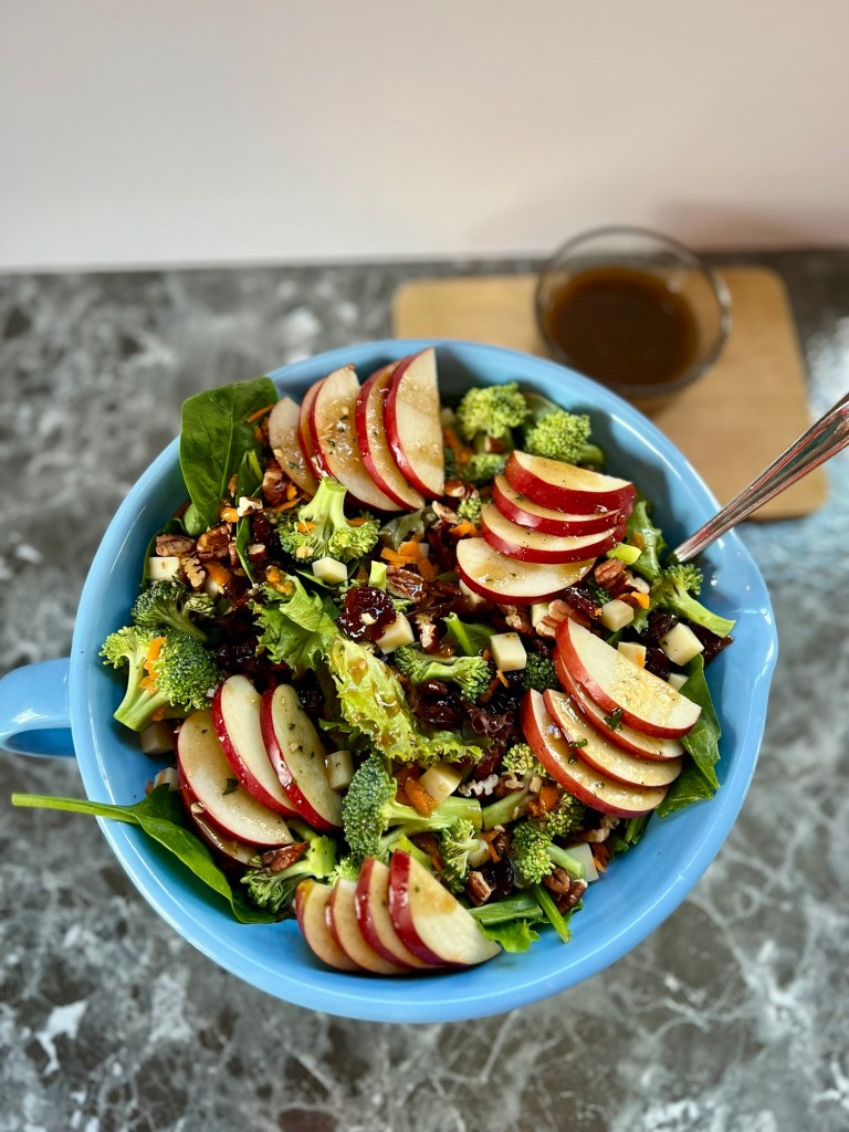Apple salad in a large blue bowl with a spoon inside and some vinaigrette behind it