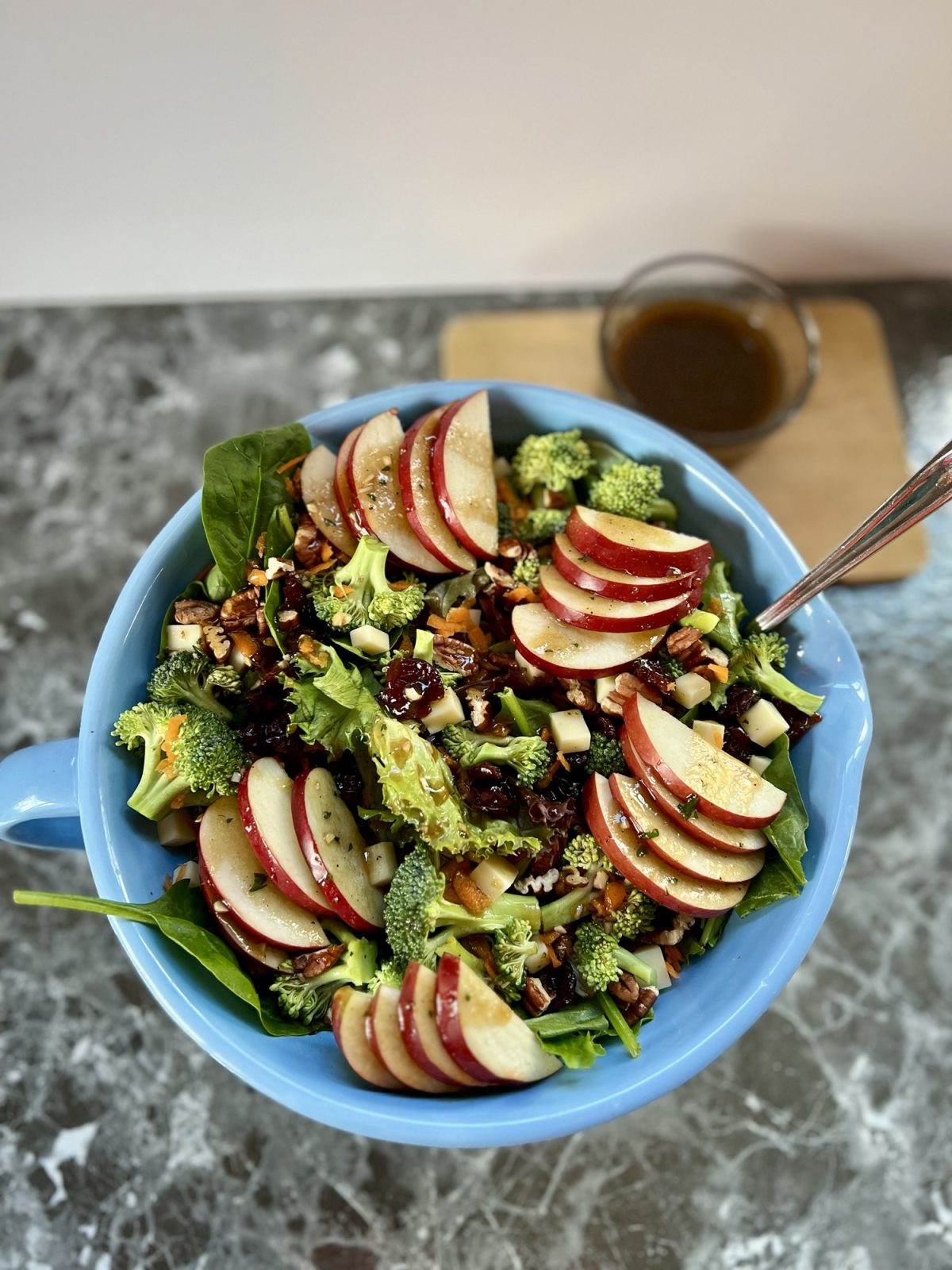 Apple salad in a large blue bowl with a spoon inside and some vinaigrette behind it