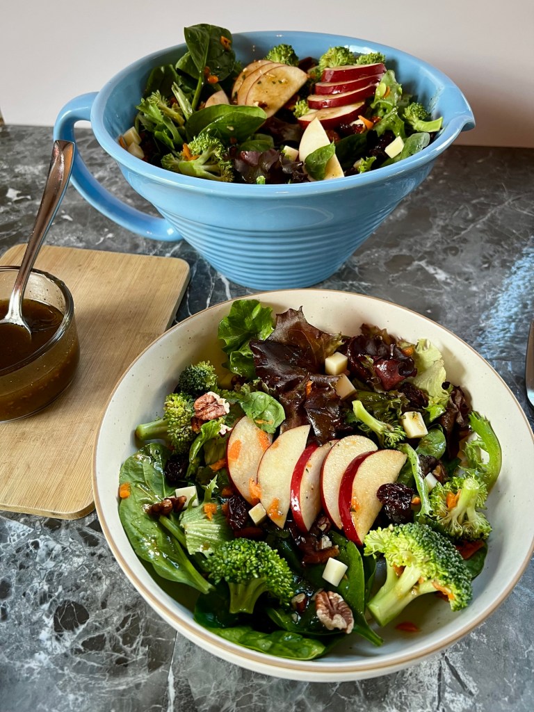 Apple salad in a white bowl with a large blue bowl behind and some dressing off to the side