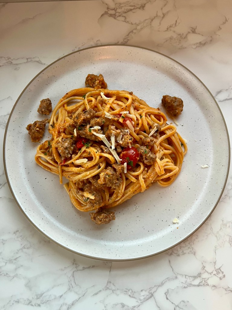 A white plate with creamy italian sausage pasta on it, with some parmesan and parsley on top