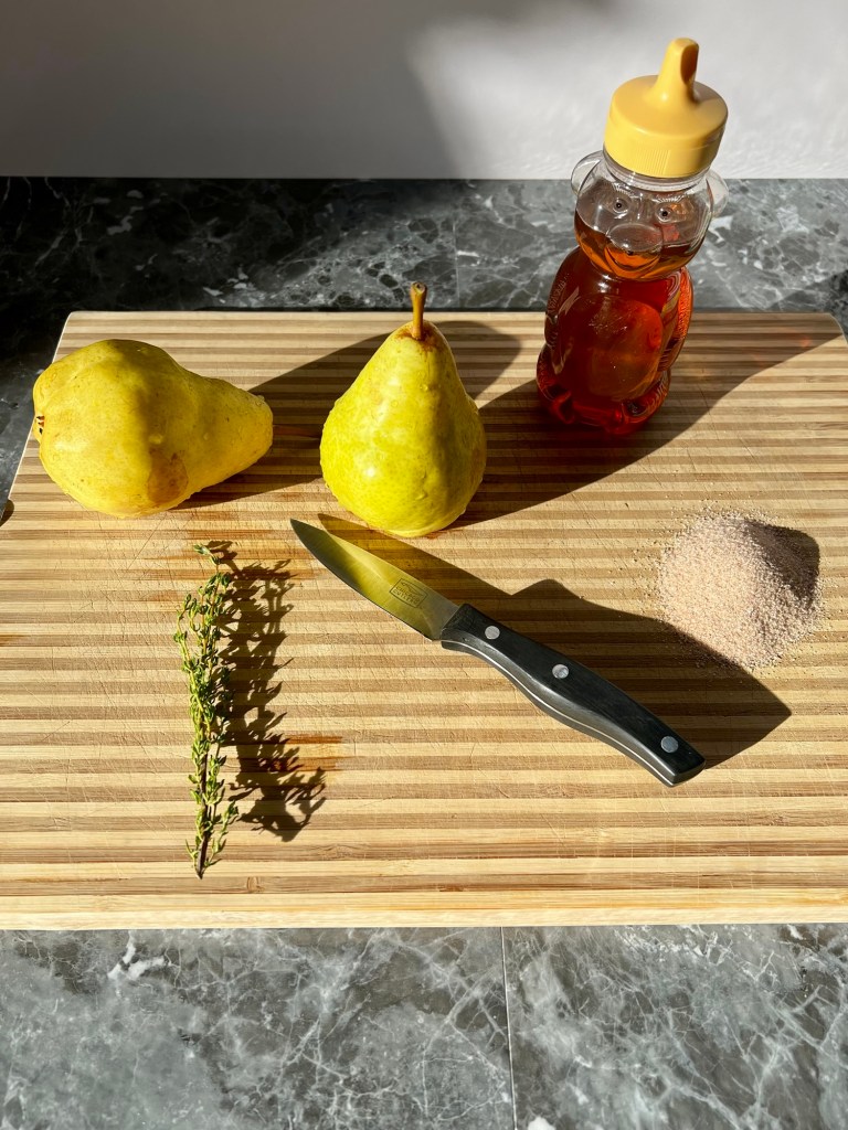Pears, thyme, honey, cinnamon, sugar, and a pairing knife on a cutting board on a countertop