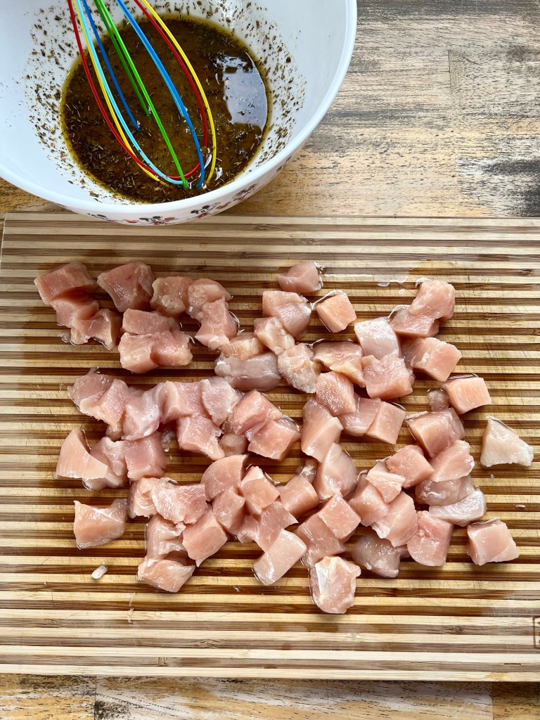 Chicken chopped up on a wooden cutting board with a bowl of marinade behind it