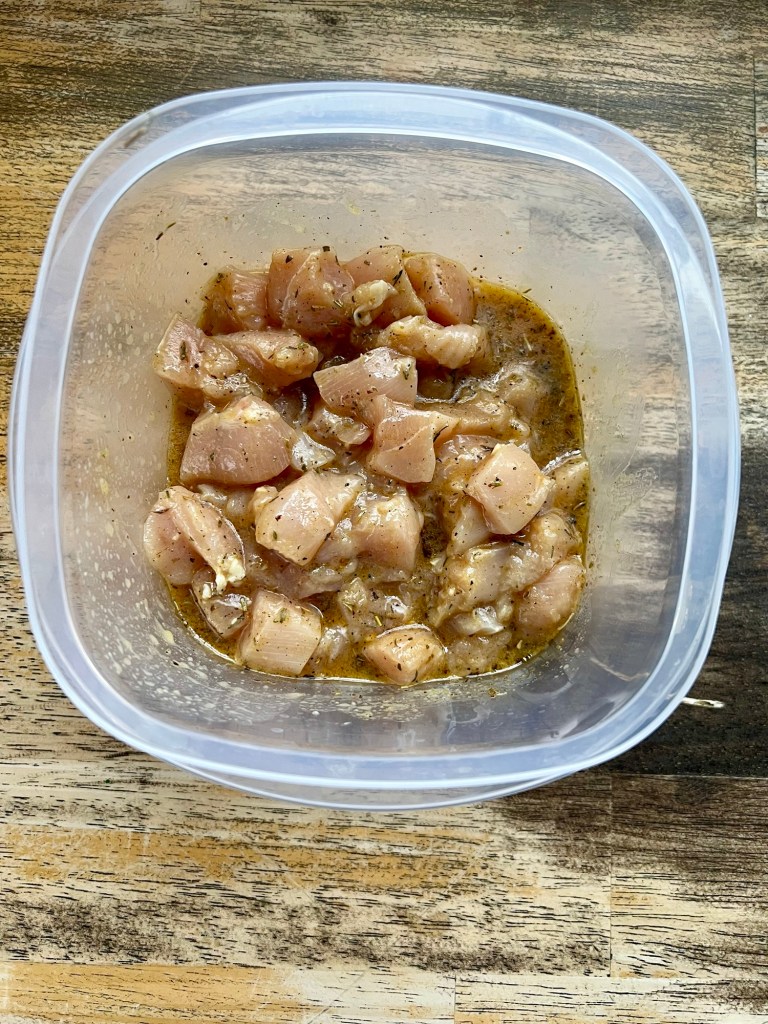 Chopped chicken in a marinade in a tupperware on a wooden table