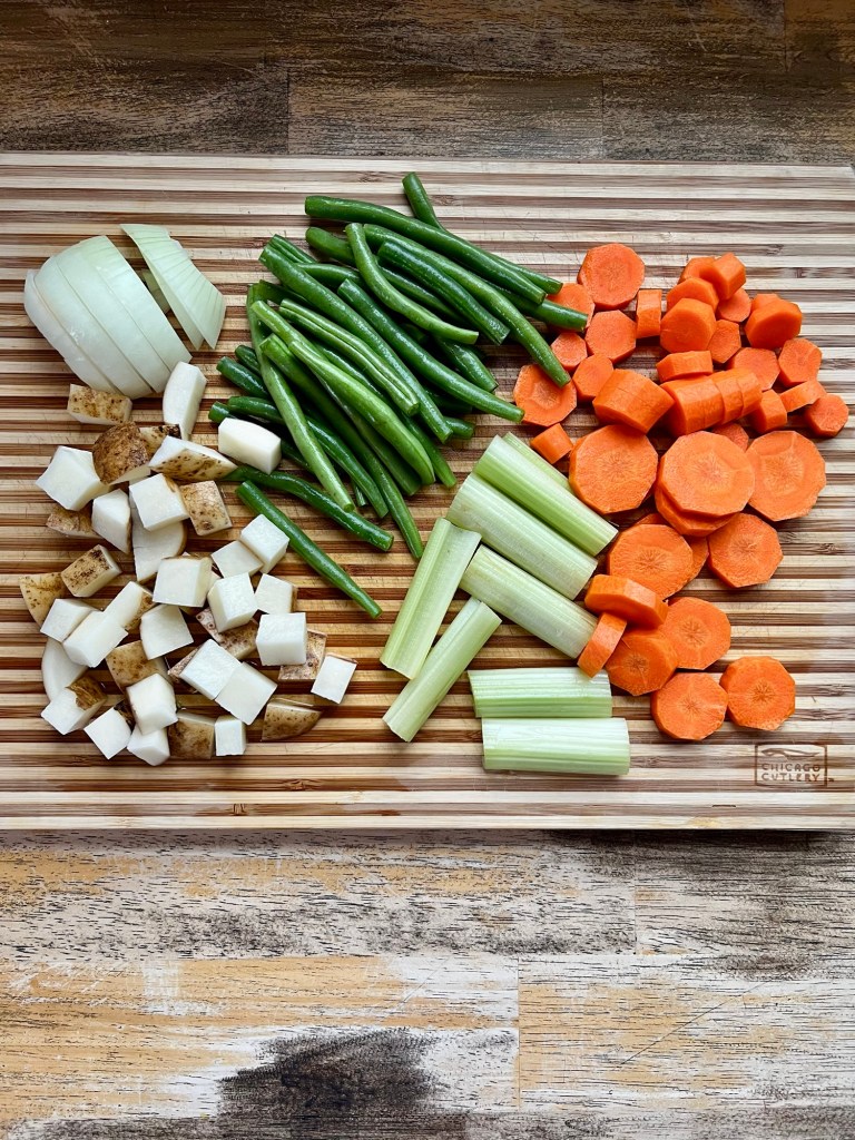 Carrots, beans, onion, potatoes, and celery chopped up on a wooden cutting board