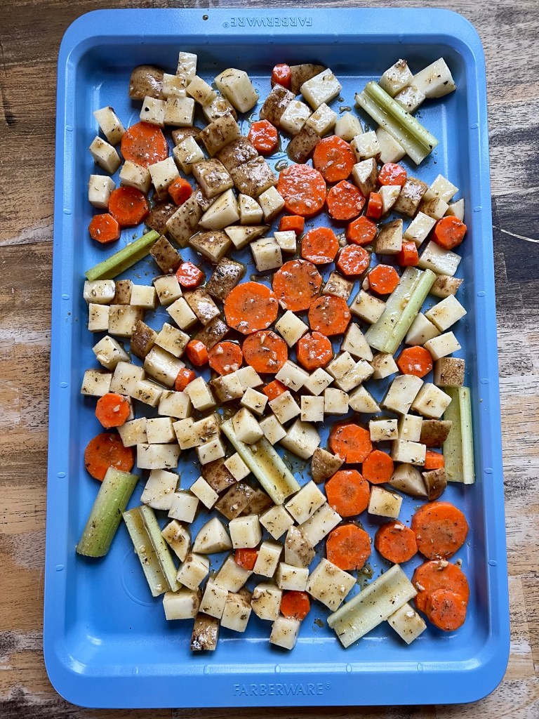 A bunch of raw marinaded veggies on a blue sheet pan before going into the oven