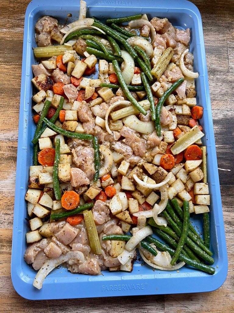 A blue sheet pan filled with chicken and veggies before going into the oven