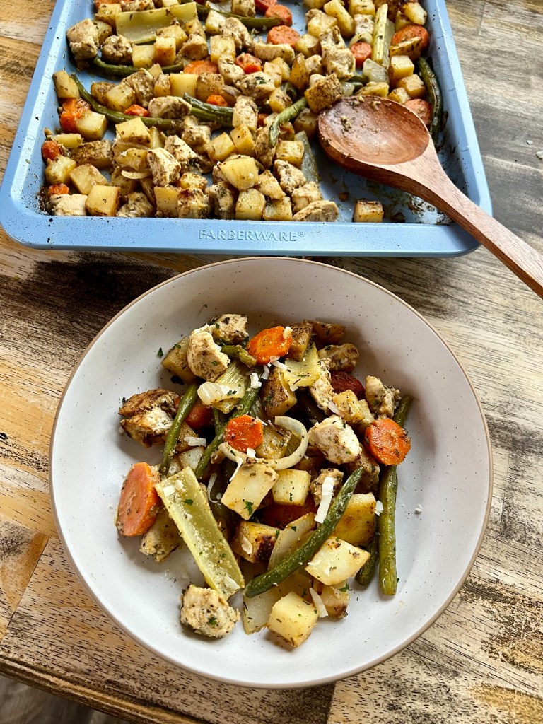 Harvest sheet pan dinner on a wooden table, with a white bowl filled with it in front of it