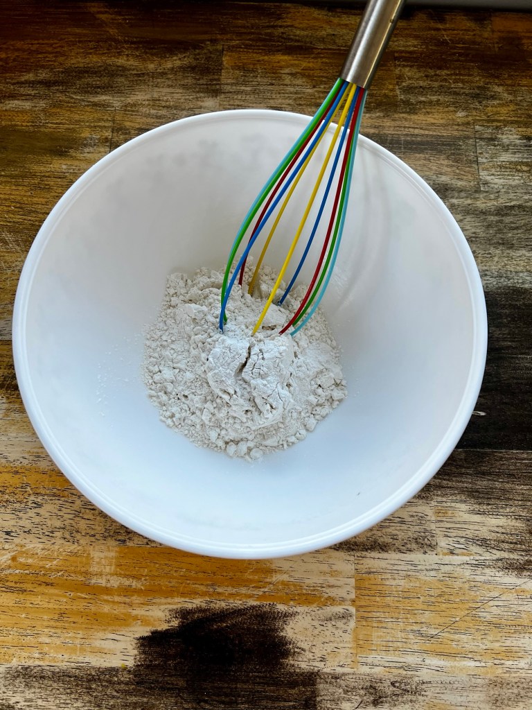 Dry ingredients for cookies in a mixing bowl with a whisk inside