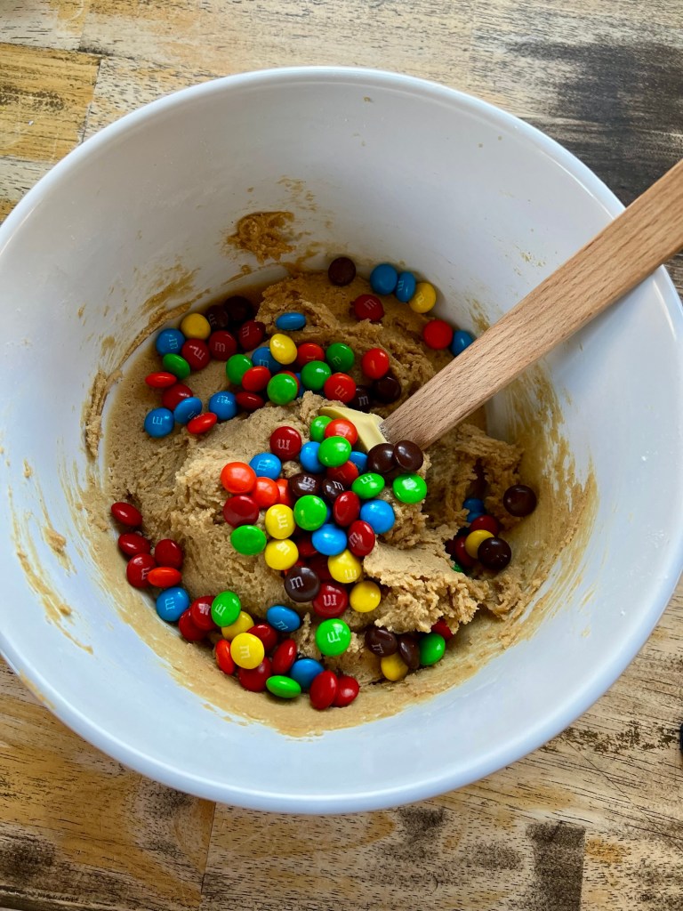Peanut butter m&m cookie mix in a bowl with a rubber spatula inside