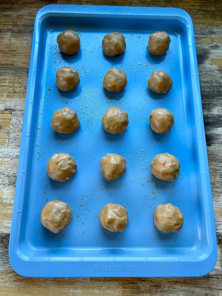 A blue baking sheet with cookie dough balls on it before being baked