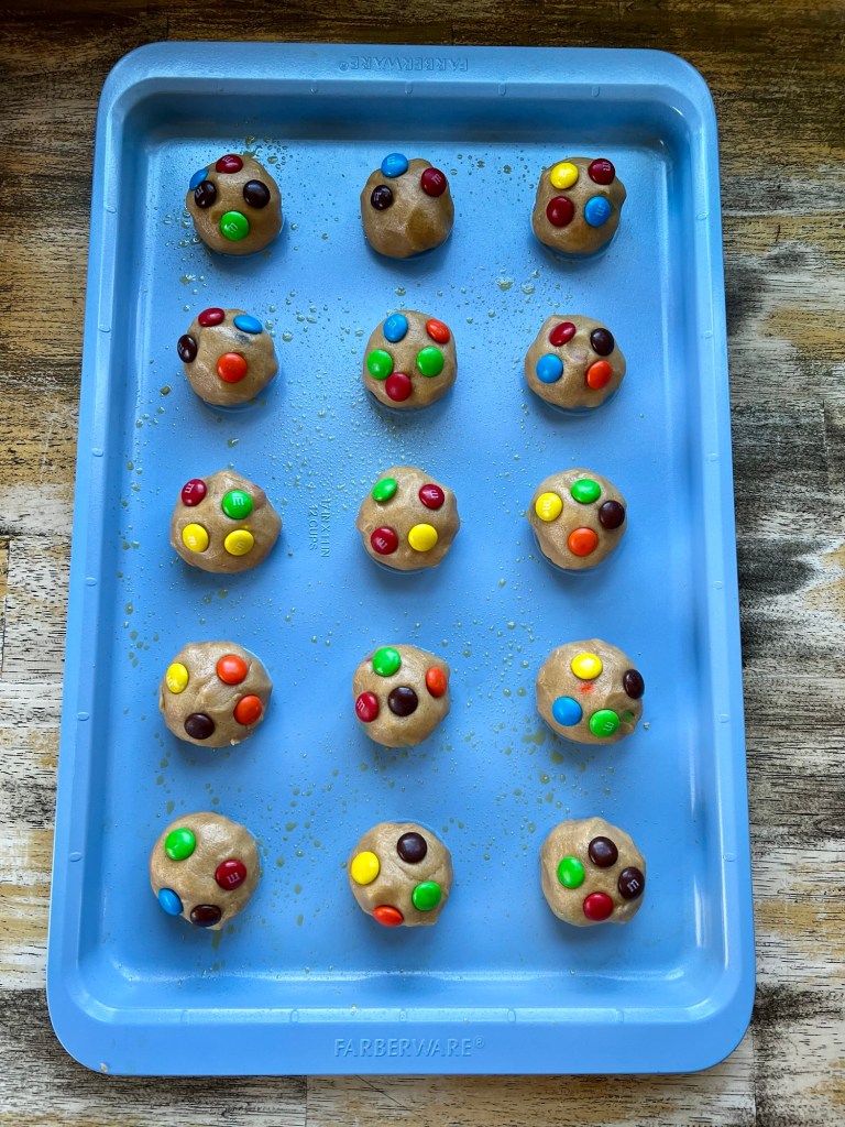A blue baking sheet with peanut butter m&m cookie dough balls on it