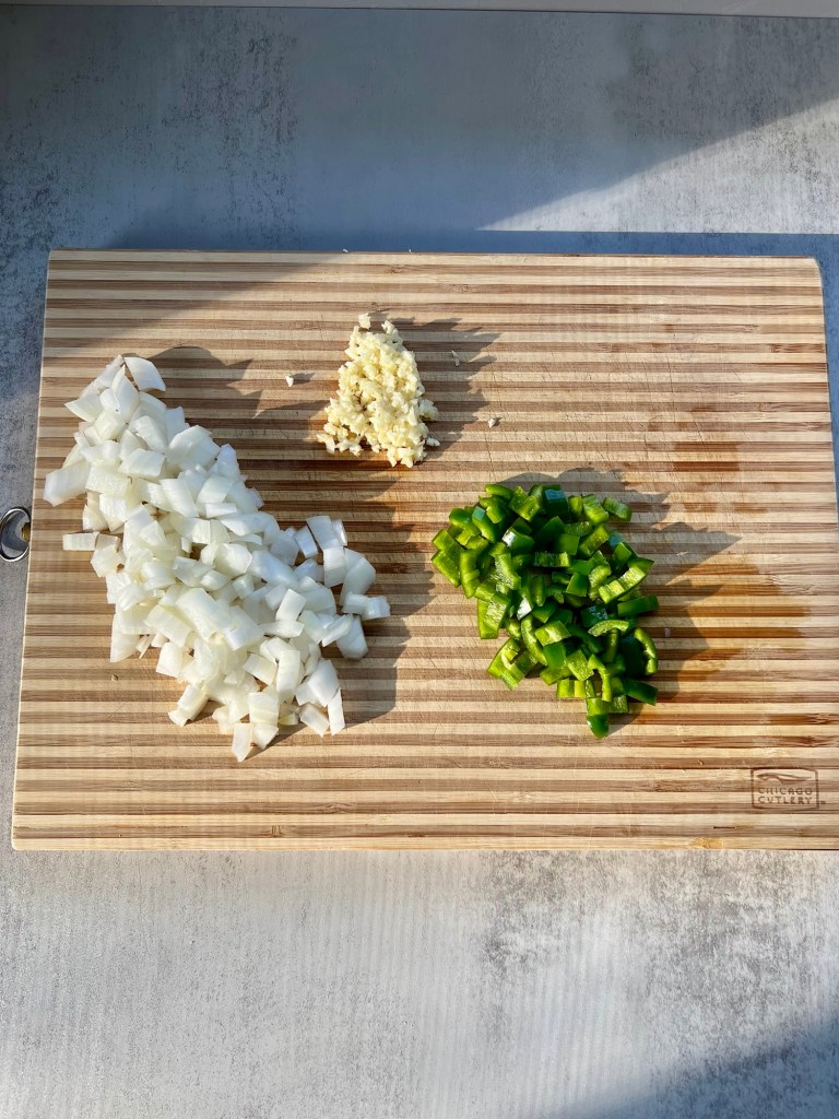 Onion, garlic, and jalapeno cut up on a wooden cutting board