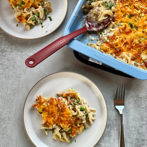 Spicy Tuna Noodle Casserole on some white plates with a big pan of it behind, with a serving spoon inside
