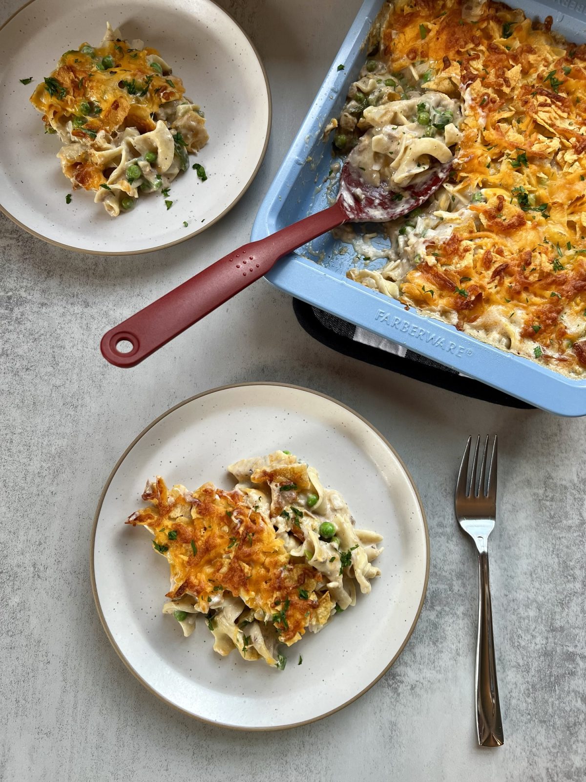 Spicy Tuna Noodle Casserole on some white plates with a big pan of it behind, with a serving spoon inside