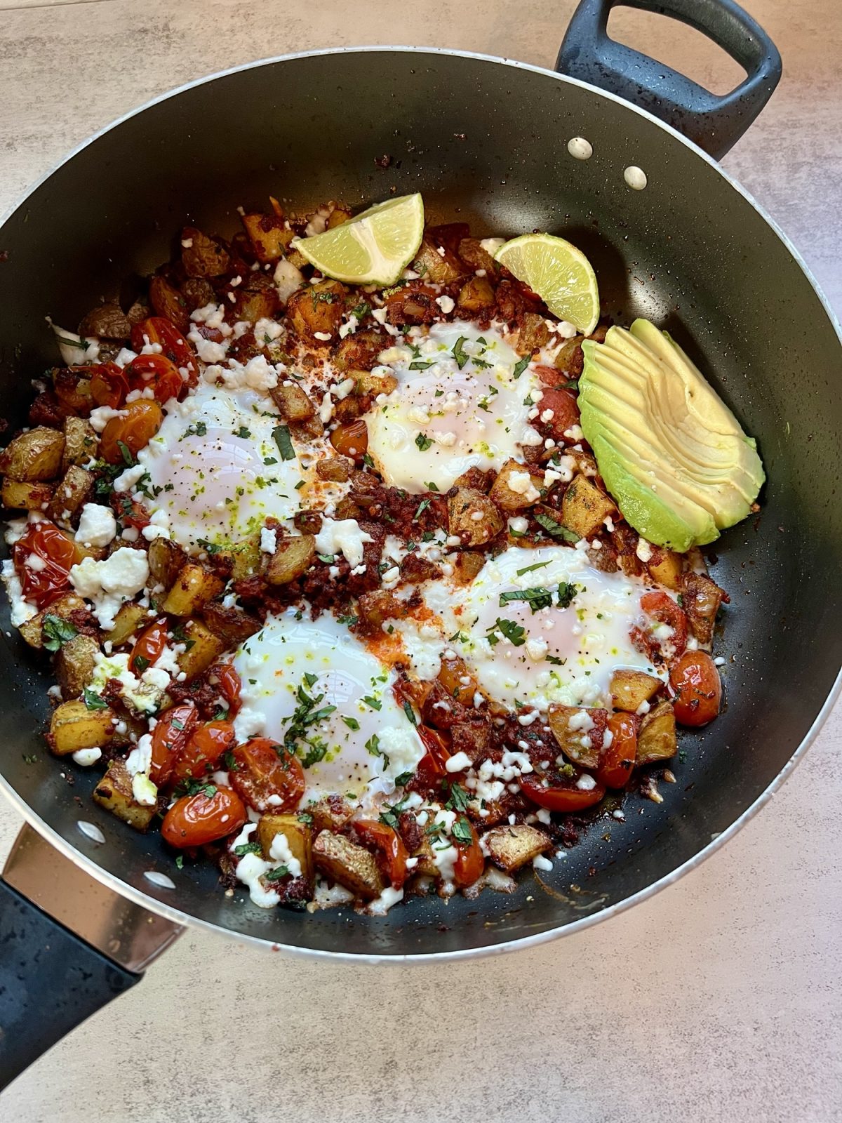 Chorizo Hash with queso fresco, cilantro, avocado, and lime wedges garnished on top