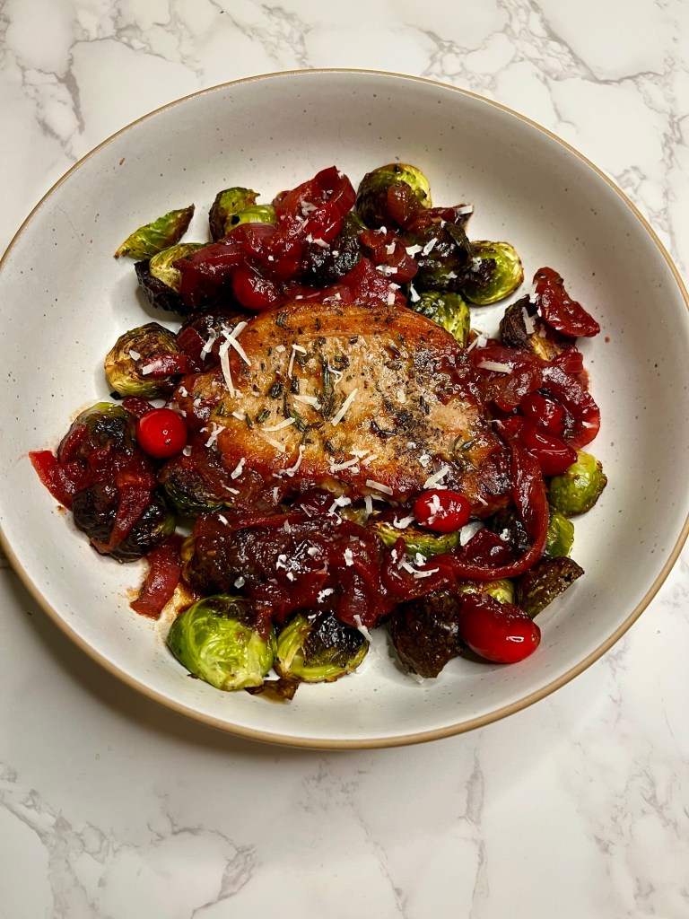 Pork chop with cranberry onion compote and brussels sprouts in a white bowl on a marble countertop