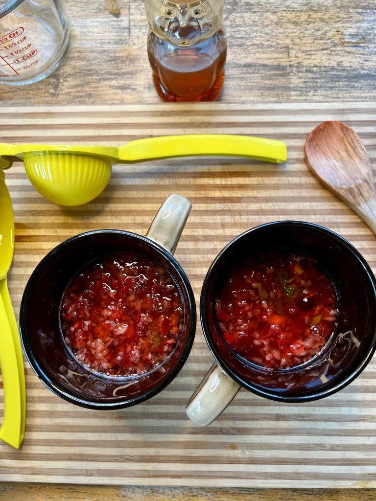 Cranberry toddies on a wooden cutting board with some honey and a lemon juicer nearby