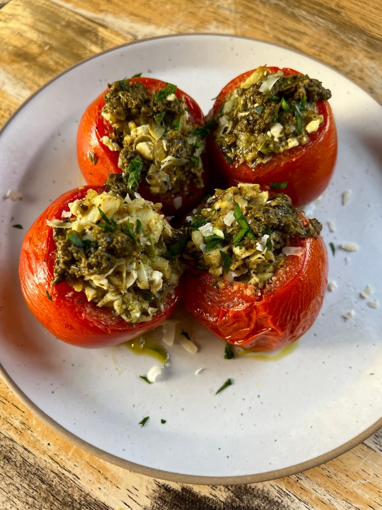 Greek Stuffed Tomatoes on a white plate with some parmesan, parsley, and pesto for garnish