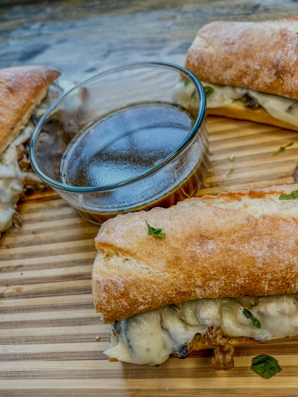 Steak Melts cut up in pieces on a wooden cutting board with some au jus next to it