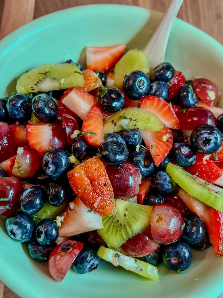 Fruit Salad in a blue bowl with a wooden spoon inside, on a wooden table