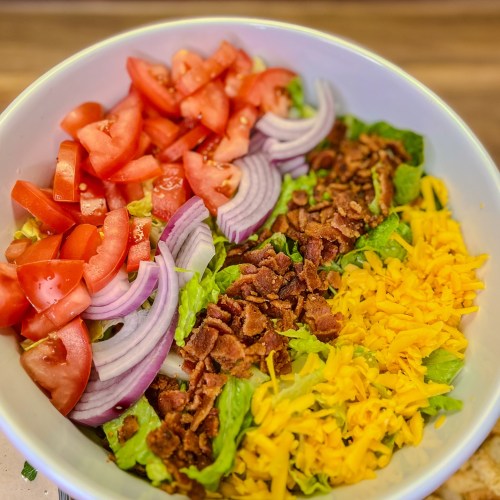 A bacon Caesar salad in a large bowl with some dressing and croutons nearby