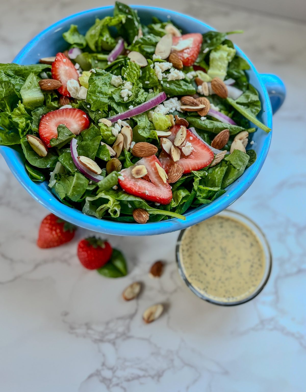 Strawberry Salad with onion, almond, and dressing next to it on a marble counter