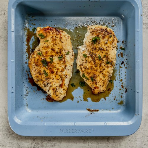 Two oven baked chicken breasts in a blue baking pan