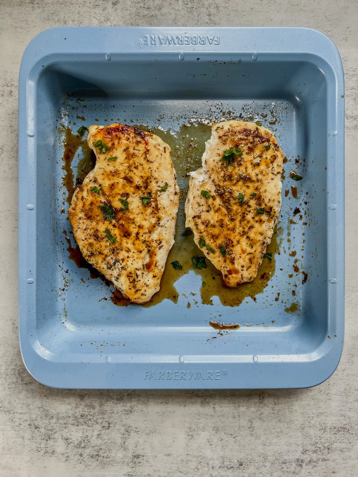 Two oven baked chicken breasts in a blue baking pan