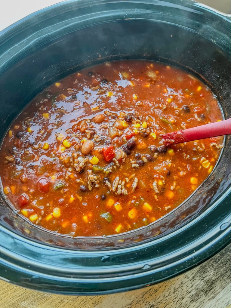Crockpot taco soup in a large crockpot on a wooden table, with a red spoon scooping some