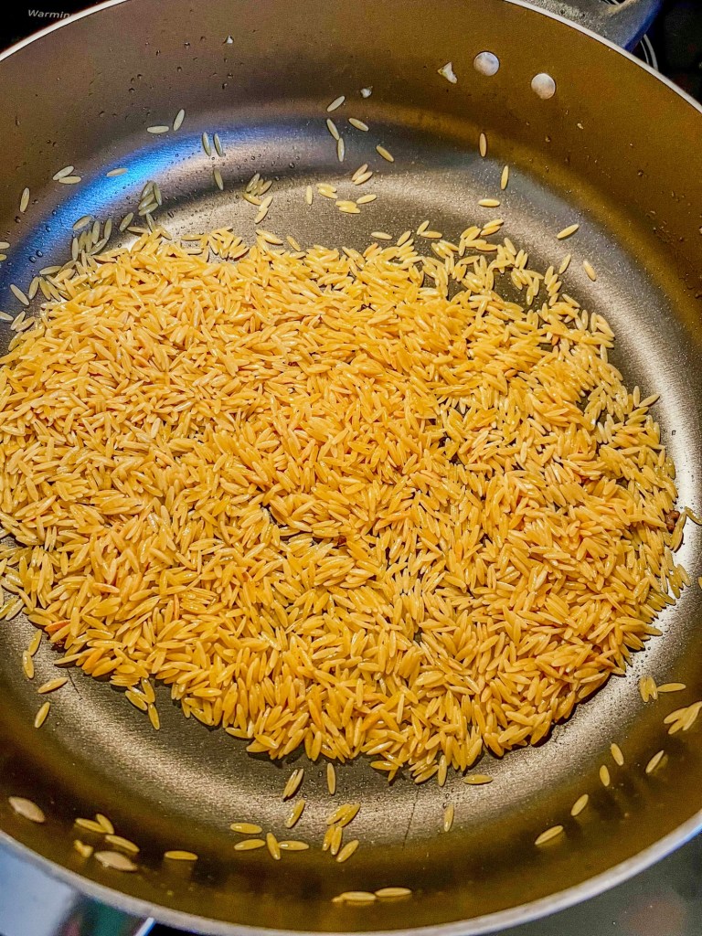 Orzo toasting in a skillet on the stove
