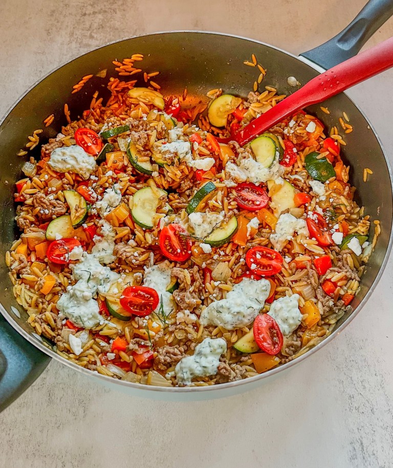 One Pot Greek Orzo in a skillet with a red serving spoon scooping some out