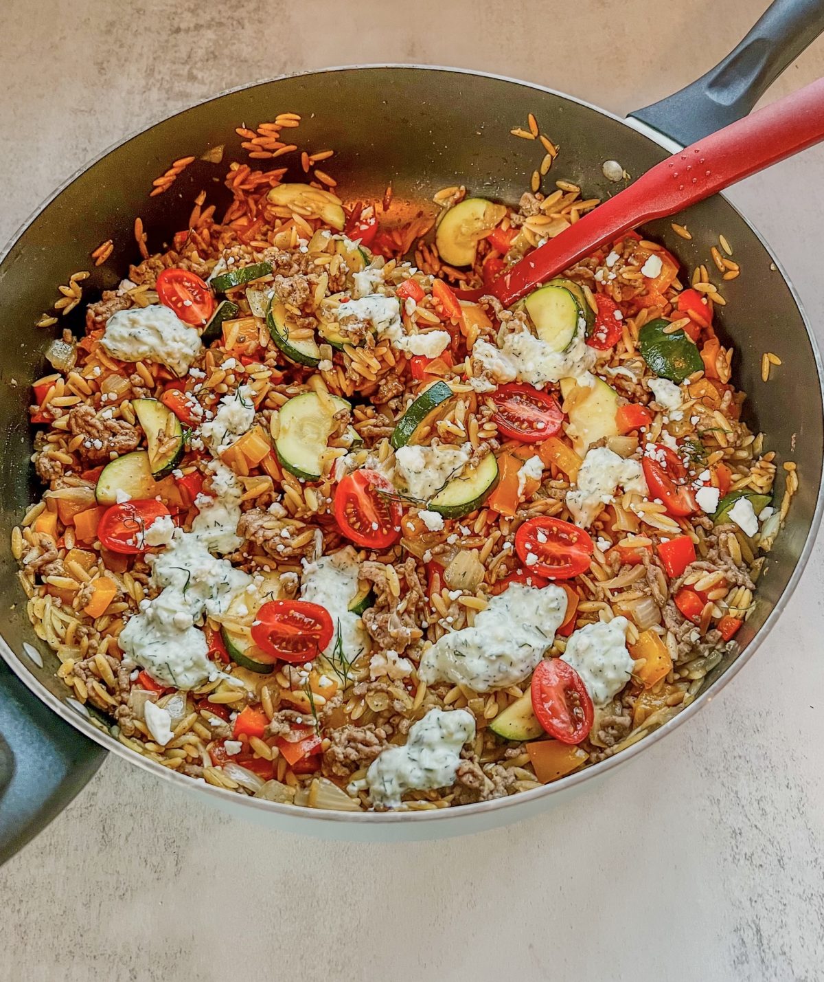 One Pot Greek Orzo in a skillet with a red serving spoon scooping some out