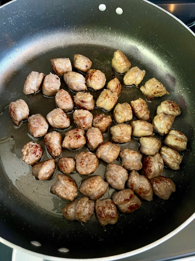 Beer brats cooking in a skillet on the stove