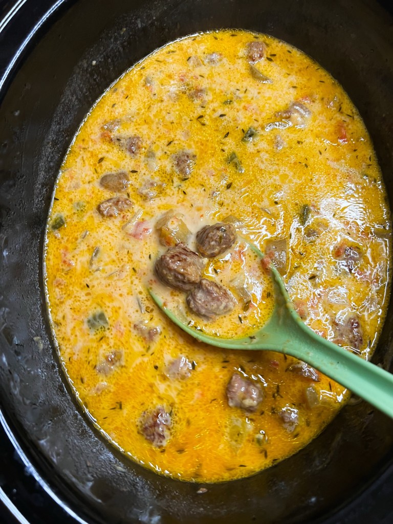 Cheesy bratwurst soup in a crockpot with a green spoon scooping some