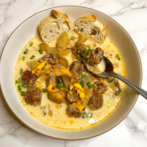 Cheesy Beer Brat Chowder in a white bowl with a spoon scooping some out