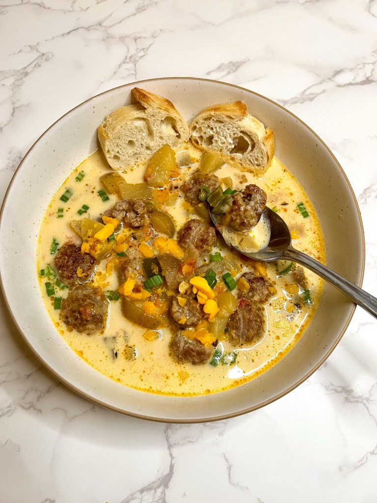 Cheesy Beer Brat Chowder in a white bowl with a spoon scooping some out