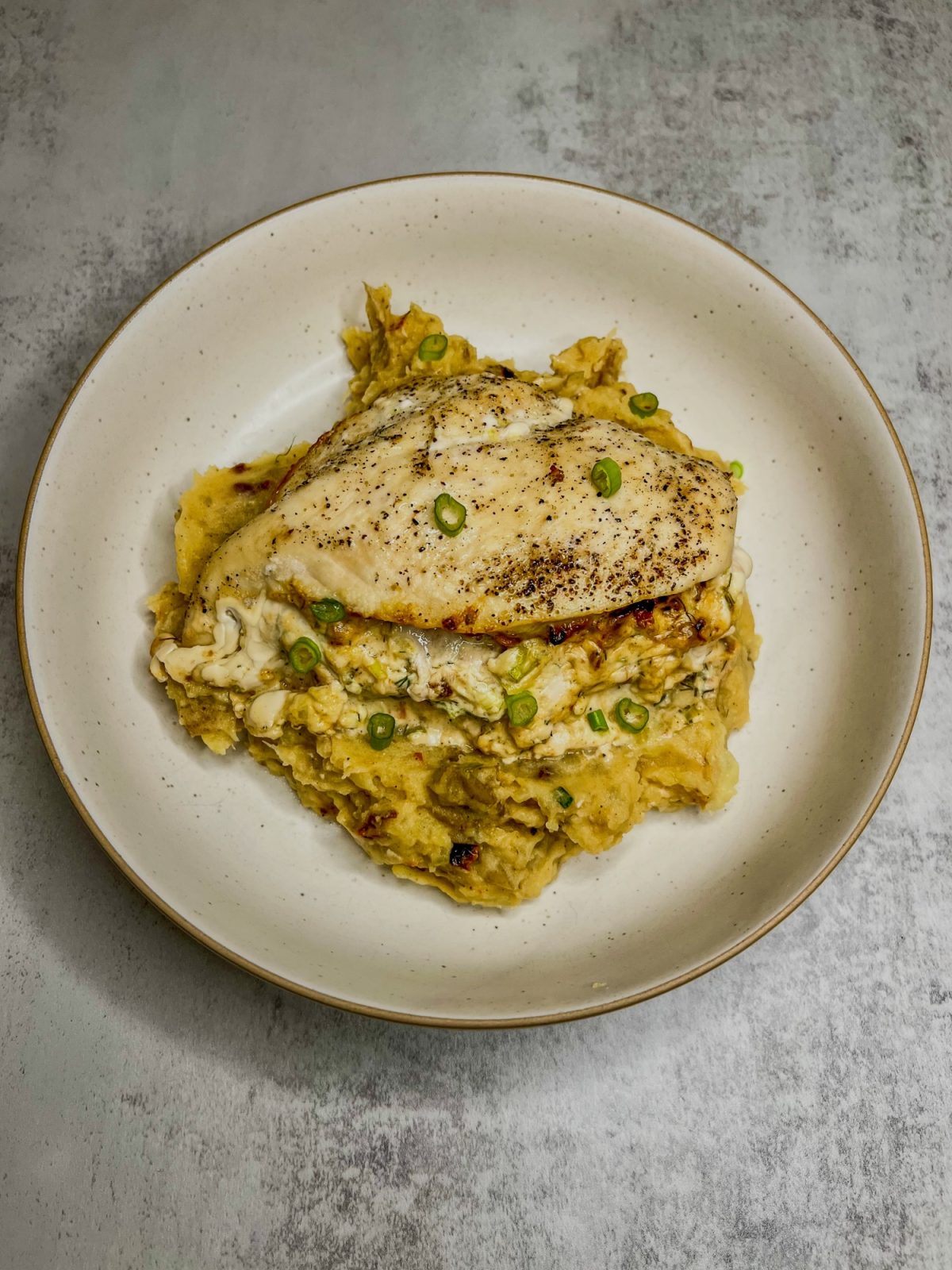 Sun-Dried Tomato Stuffed Chicken Breast over a bed of mashed potatoes, on a white plate