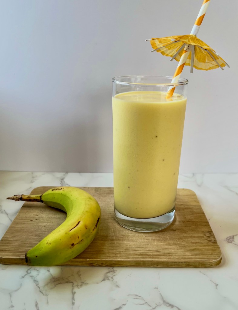 A mango banana smoothie on a cutting board with a banana next to it