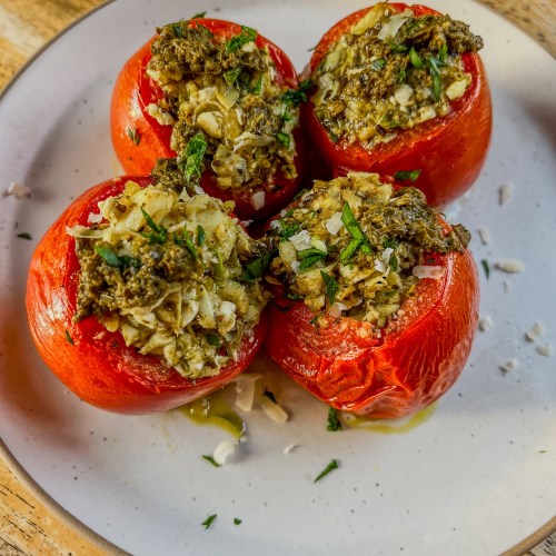 Greek Stuffed Tomatoes on a white plate with some parmesan, parsley, and pesto for garnish