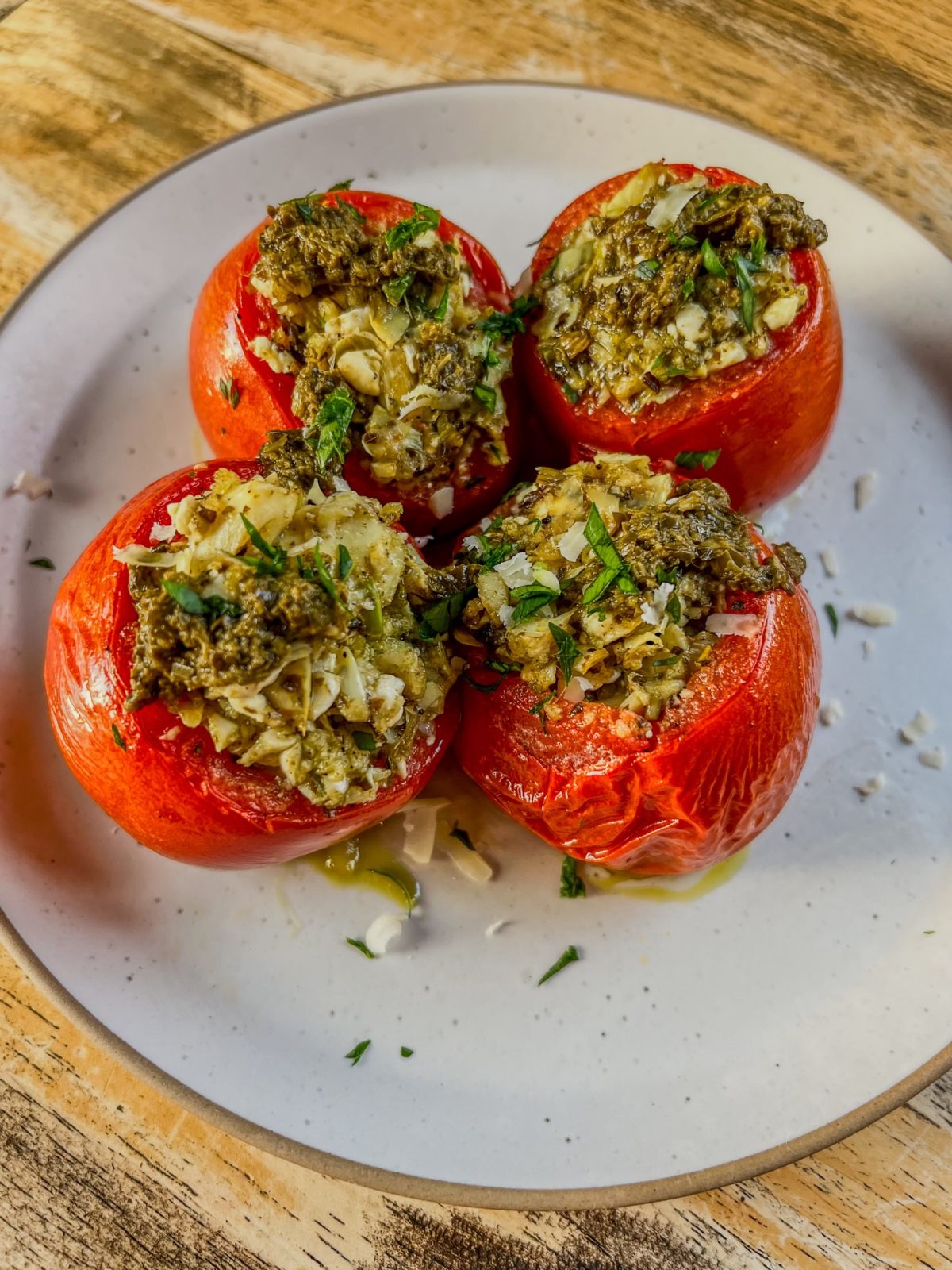 Greek Stuffed Tomatoes on a white plate with some parmesan, parsley, and pesto for garnish