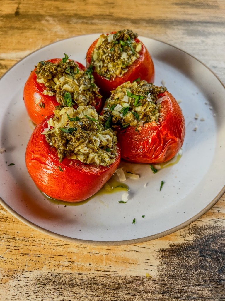 Greek Stuffed Tomatoes on a white plate with some parmesan, parsley, and pesto for garnish