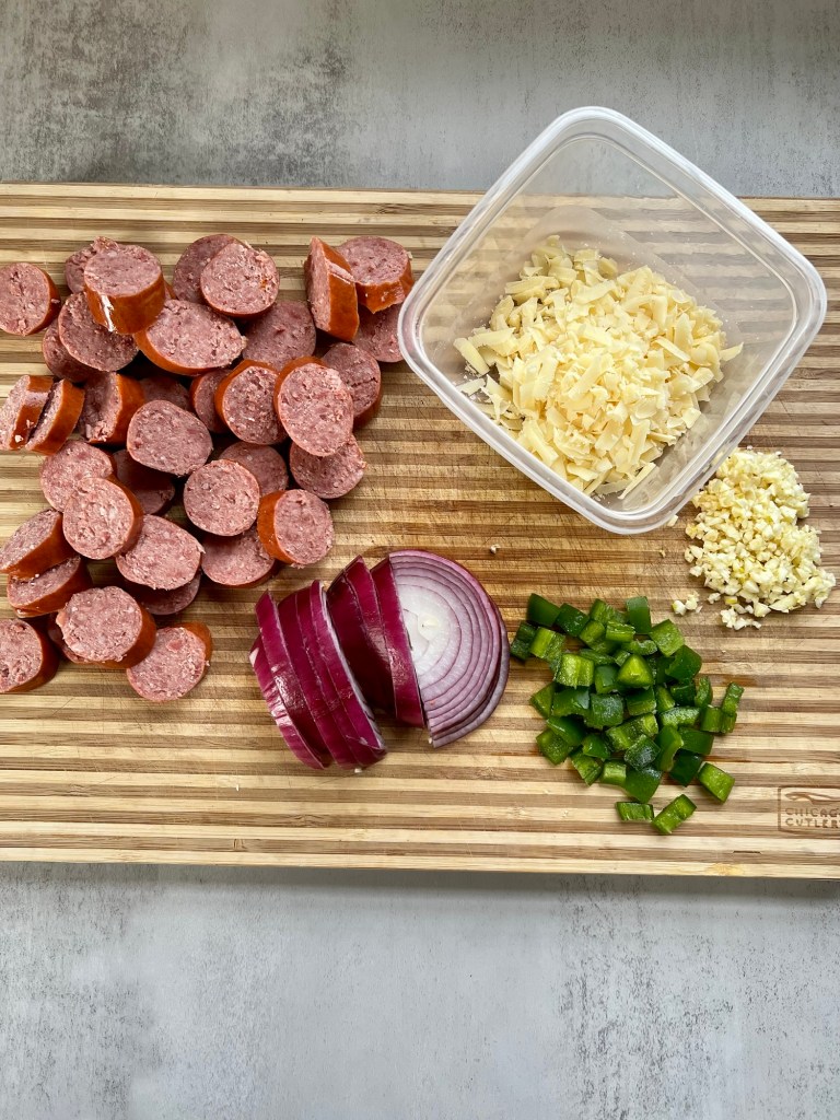 Sausage, veggies, and shredded cheese on a wooden cutting board