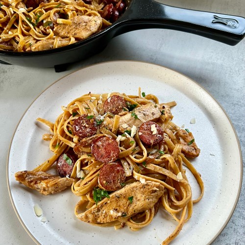 Sausage Chicken Cajun Pasta on a white plate with a pan filled with more of it behind