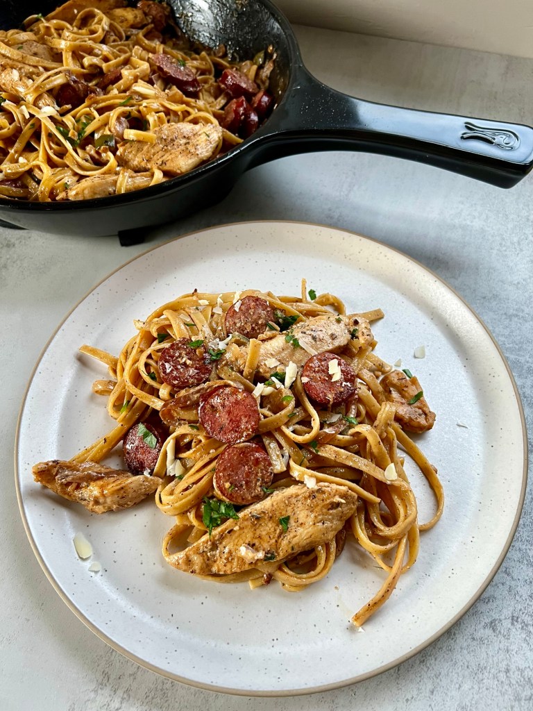 Sausage Chicken Cajun Pasta on a white plate with a pan filled with more of it behind