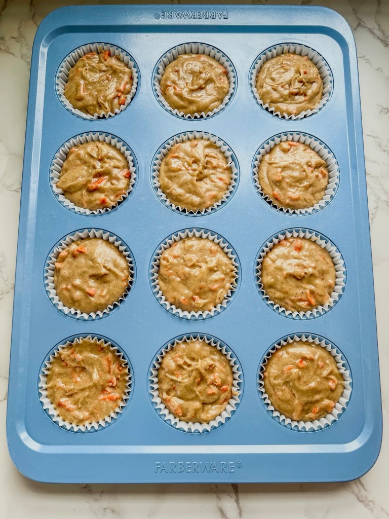 Carrot muffin batter in liners in a muffin pan just before baking