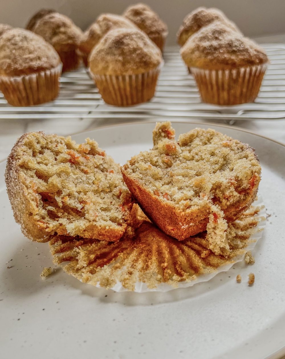 Carrot Crumble Muffins on a rack with a plate in front of it with a muffin cut in half